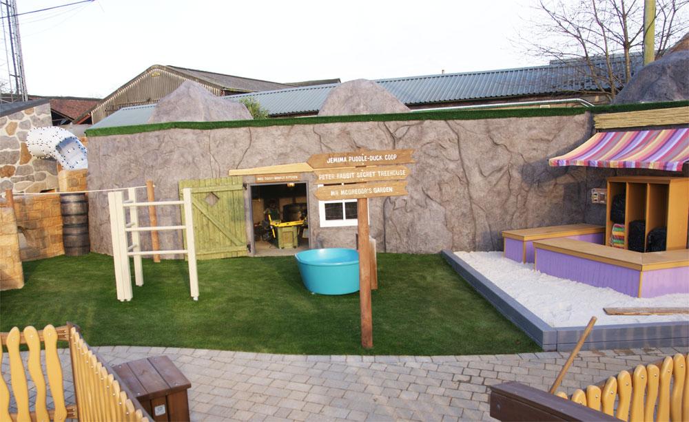Artificial grass around themed buildings and play features at the Peter Rabbit Adventure Playground