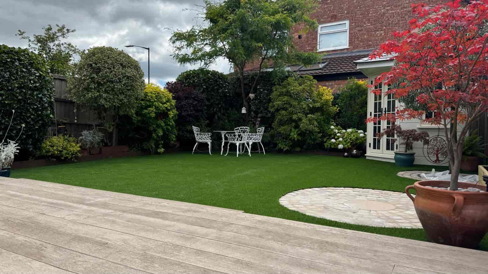 Artificial lawn with planted borders, garden seating and curved paving in Sale